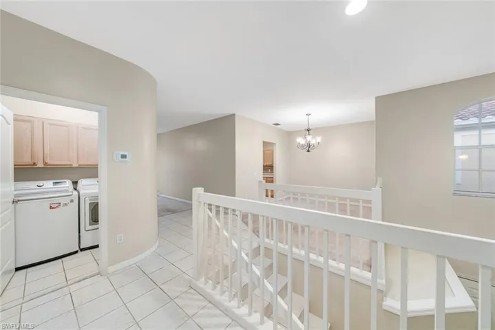 Corridor with light tile patterned floors, an upstairs landing, a chandelier, and independent washer and dryer
