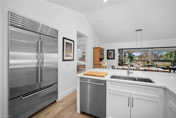 Kitchen with stainless steel appliances, vaulted ceiling, white cabinets, light wood-style flooring, and light stone counters
