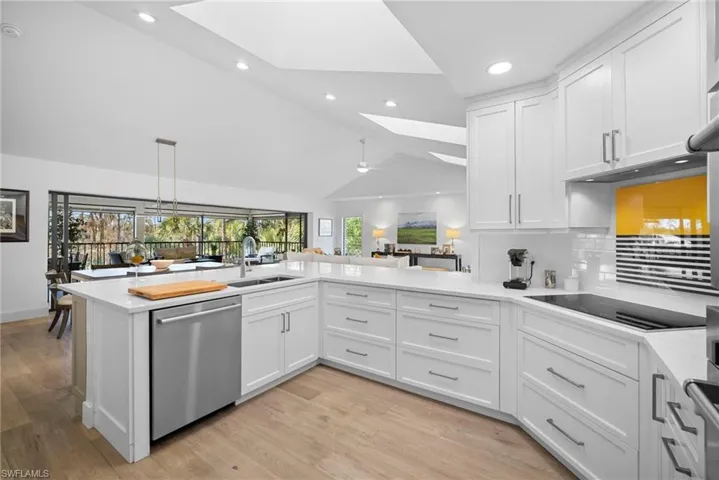 Kitchen with white cabinetry, dishwasher, light wood-style flooring, lofted ceiling, and decorative backsplash