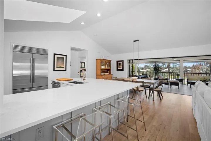 Kitchen with built in fridge, light wood-style flooring, pendant lighting, light stone counters, and a high ceiling