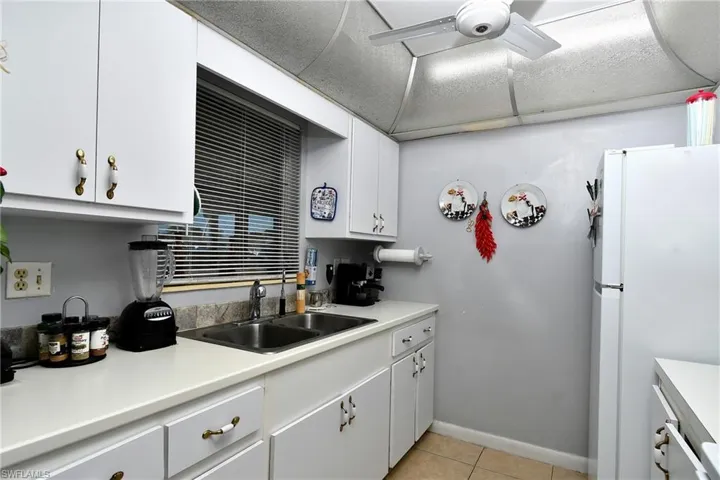 White cabinetry with decorative hardware, a dual basin stainless steel sink, a tile backsplash, and light-colored countertops