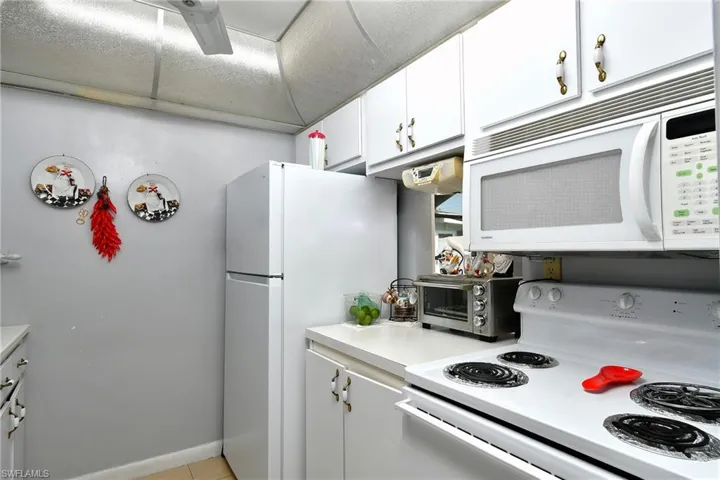 Compact kitchen featuring white cabinetry, white appliances, and light-toned countertops