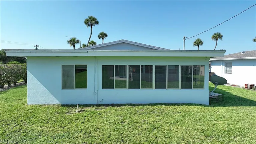 Exterior featuring light blue stucco finish, a covered patio with multiple windows, and a green lawn