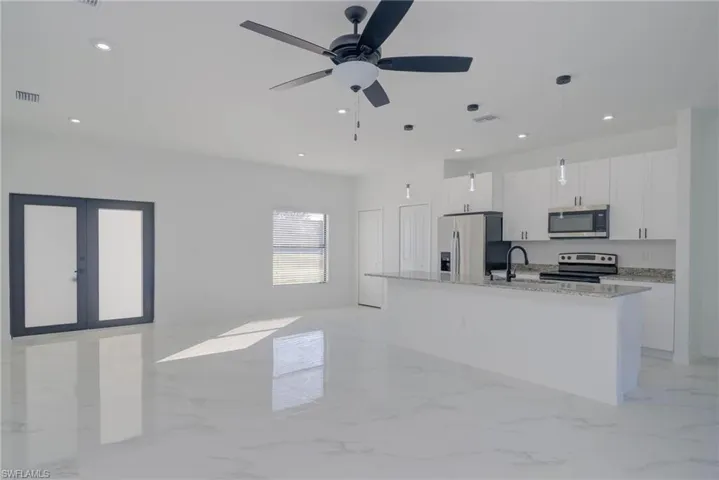 Kitchen featuring a center island with sink, appliances with stainless steel finishes, light stone countertops, pendant lighting, and white cabinetry
