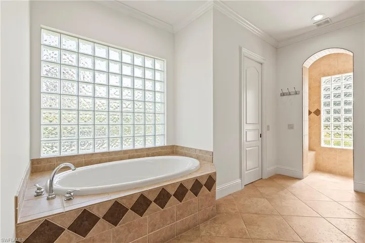 Primary Bathroom with tiled soaking tub, tile patterned flooring, and crown molding