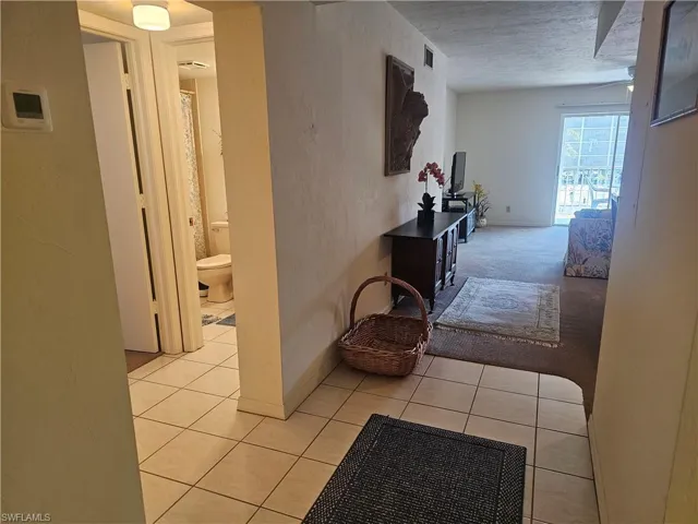 Hall featuring light tile patterned floors, a textured ceiling, and light carpet
