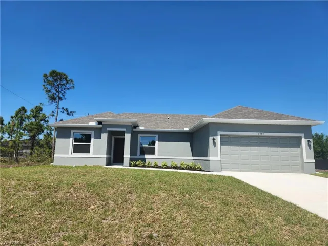 View of front of house with stucco siding, a front lawn, a garage, and driveway