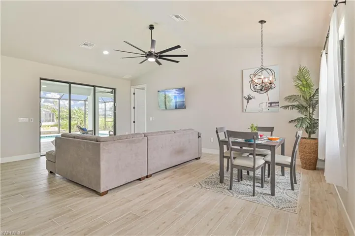 Living room featuring ceiling fan with notable chandelier, vaulted ceiling, and light hardwood / wood-style floors