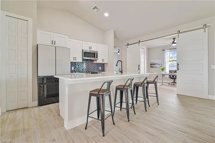 Kitchen with a kitchen island with sink, refrigerator, white cabinets, a barn door, and a kitchen bar