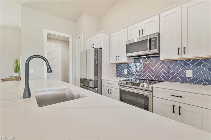 Kitchen featuring sink, light stone counters, stainless steel appliances, backsplash, and white cabinetry