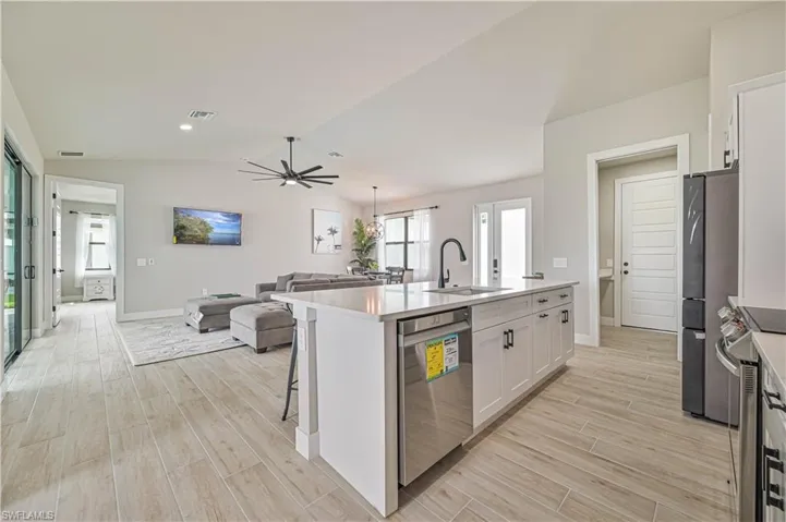 Kitchen featuring an island with sink, lofted ceiling, sink, white cabinetry, and appliances with stainless steel finishes