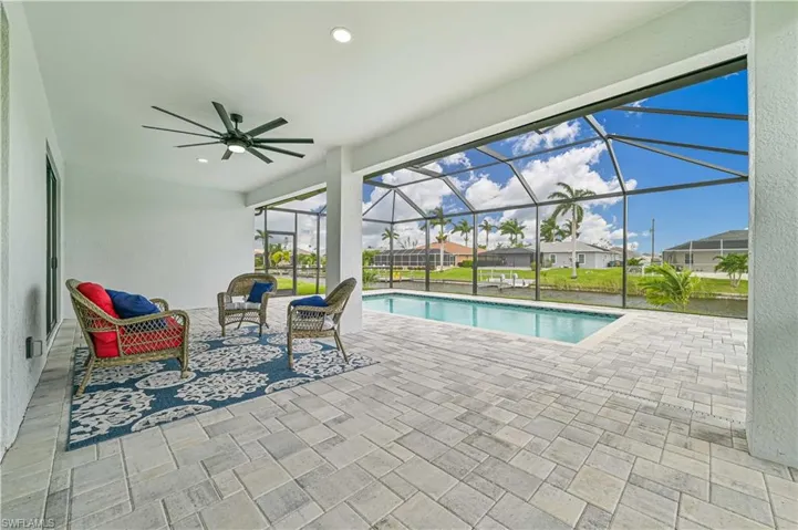View of pool with glass enclosure, ceiling fan, and a patio area