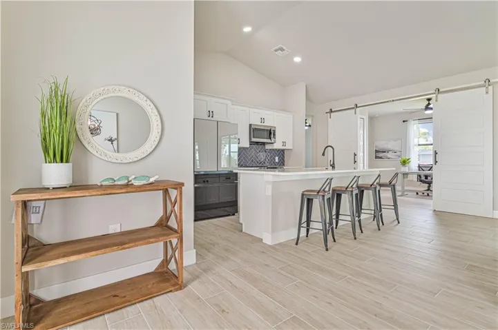 Kitchen with an island with sink, a breakfast bar, a barn door, vaulted ceiling, and white cabinetry