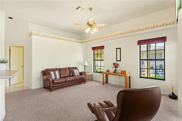 Living area featuring ceiling fan, ornate columns, light tile patterned flooring, french doors, and a wainscoted wall