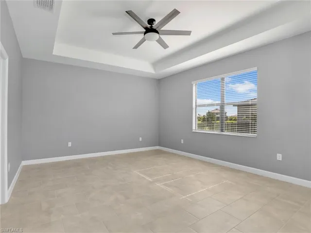 Primary Bedroom with a tray ceiling, a ceiling fan, and baseboards