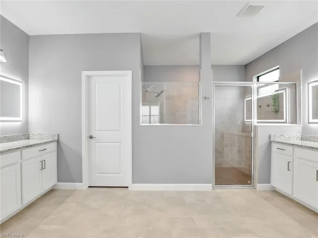 Full bath with a shower stall, two vanities, and baseboards