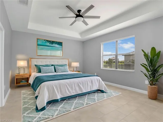 Bedroom with a raised ceiling, baseboards, light tile patterned flooring, and ceiling fan
