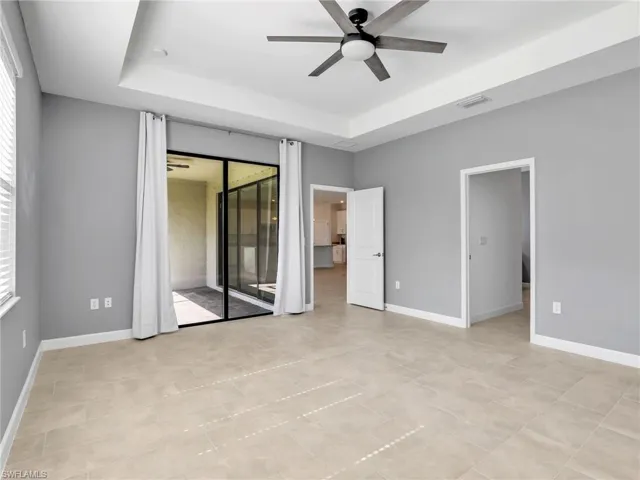 Unfurnished bedroom featuring a raised ceiling, access to exterior, baseboards, and a ceiling fan