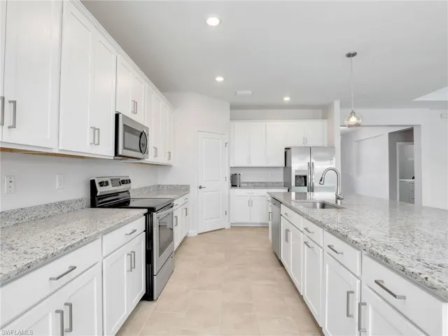 Kitchen with stainless steel appliances, a sink, white cabinets, hanging light fixtures, and light stone countertops
