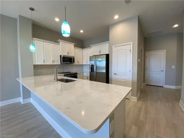 Kitchen featuring light wood finished floors, a peninsula, a sink, stainless steel appliances, and white cabinetry