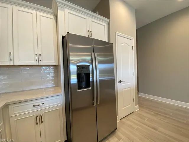 Kitchen with tasteful backsplash, white cabinetry, stainless steel fridge with ice dispenser, light wood finished floors, and baseboards