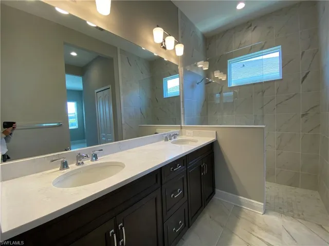 Full bathroom featuring double vanity, a walk in shower, marble finish floor, and a sink