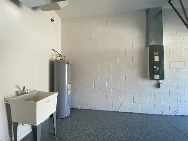 Utility room with electric panel, water heater, and a sink