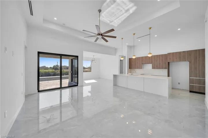 Unfurnished living room featuring a raised ceiling, light marble finish flooring, ceiling fan, and a chandelier