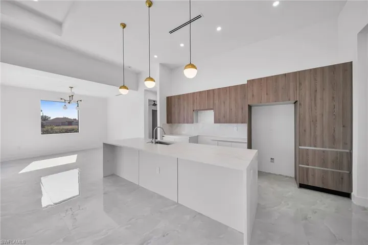 Kitchen featuring wood finish cabinets, light stone countertops, modern cabinets, a kitchen island with sink, and pendant lighting