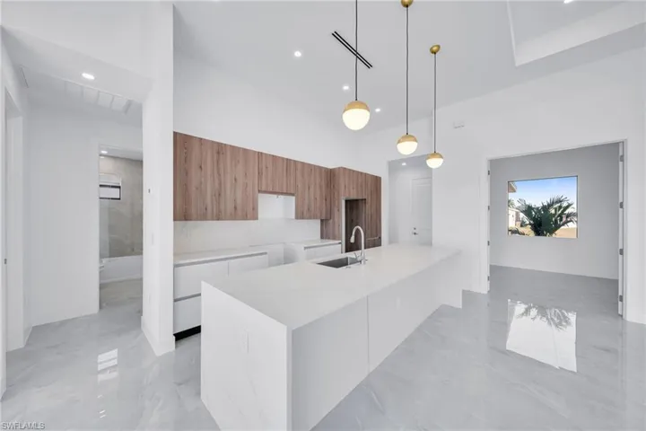 Two tone kitchen with modern cabinets, light stone countertops, hanging light fixtures, light marble finish floors, and two tone color scheme