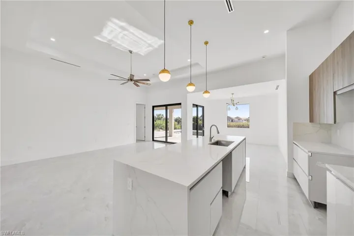 Kitchen featuring modern cabinets, a chandelier, light stone countertops, a kitchen island with sink, and a high ceiling
