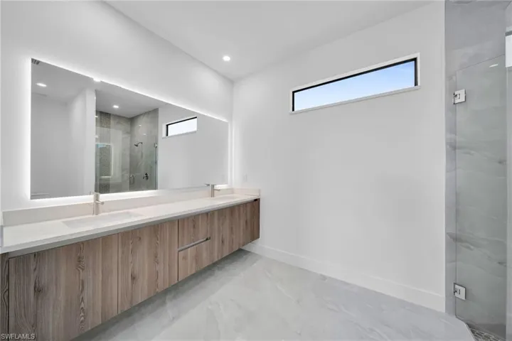 Full bath with double vanity, a marble finish shower, finished concrete flooring, and recessed lighting