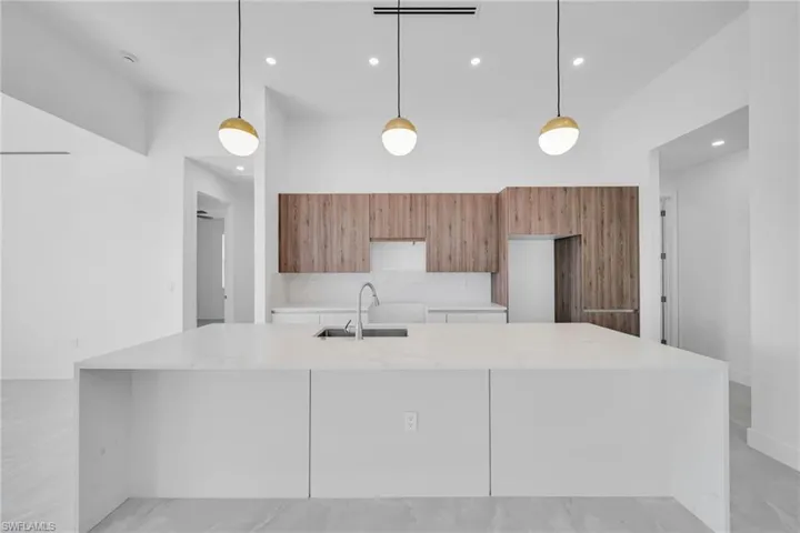 Kitchen with modern cabinets, light stone counters, pendant lighting, wood finish cabinets, and a large island with sink