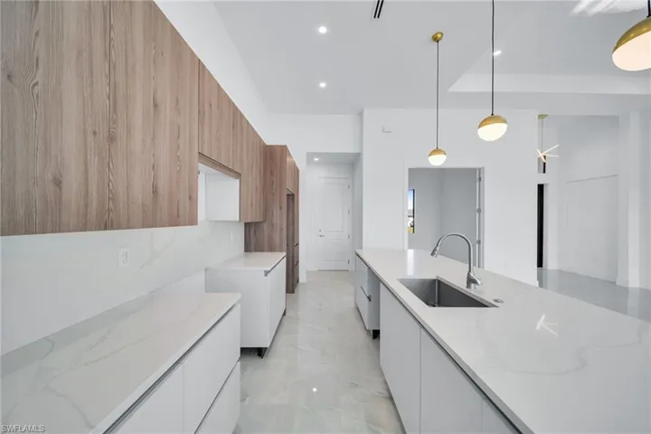Kitchen with modern cabinets, light stone countertops, decorative light fixtures, light marble finish floors, and dual tone cabinets