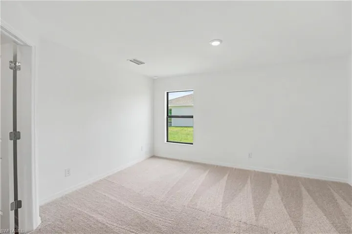 Spacious room featuring neutral carpeting, a single window, white walls, and a recessed ceiling light
