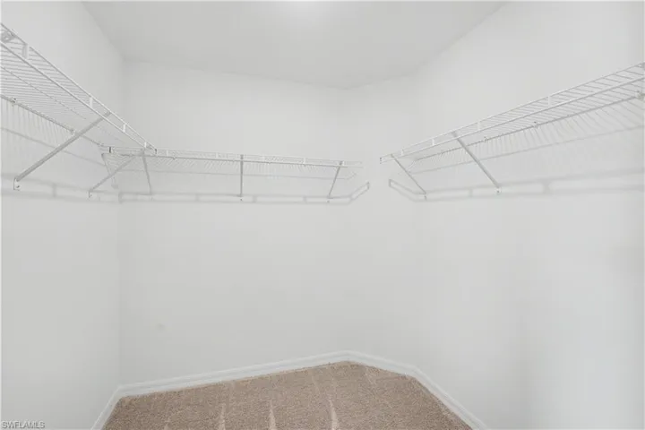 Walk-in closet featuring white wire shelving units and light brown carpet flooring