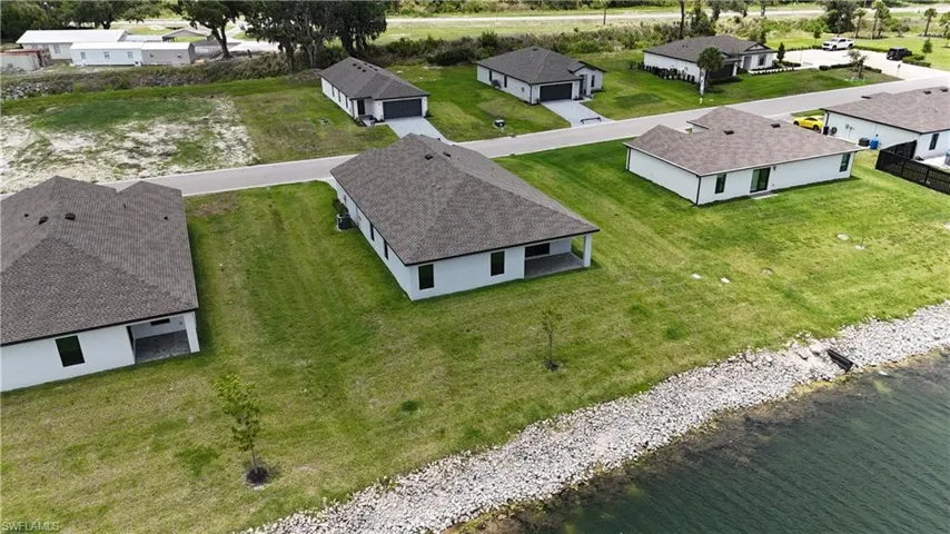 Newly constructed waterfront property featuring a white stucco exterior, dark shingle roof, and a covered patio