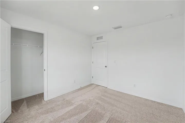 Interior room with textured carpet flooring, white walls, and a recessed ceiling light