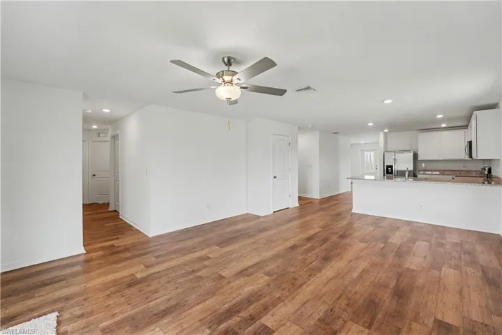 Open-concept living space featuring wood-finish flooring, a ceiling fan with integrated lighting, recessed lighting, and a kitchen with white cabinetry, stainless steel appliances, and a breakfast bar