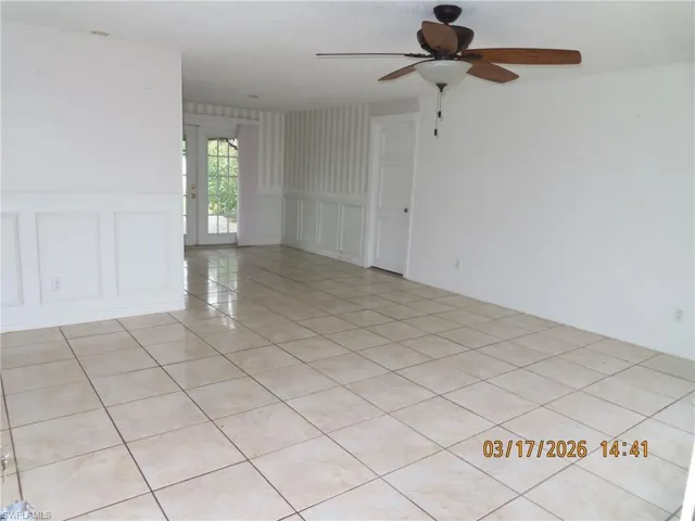 Spare room with wainscoting, french doors, a decorative wall, a ceiling fan, and light tile patterned flooring
