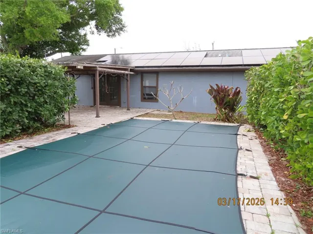 Rear view of property with roof mounted solar panels, a patio, stucco siding, and a covered pool