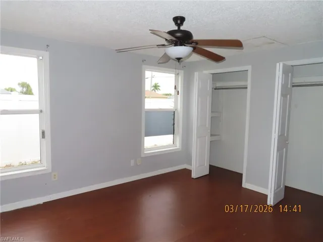 Unfurnished bedroom with multiple closets, ceiling fan, dark wood finished floors, and a textured ceiling