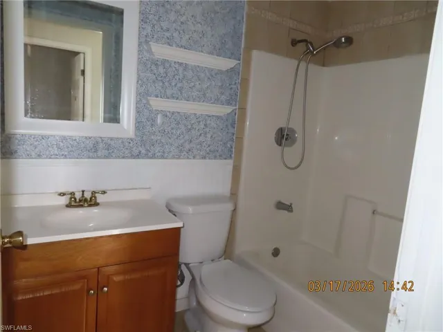 Bathroom featuring vanity, wallpapered walls, bathtub / shower combination, and wainscoting