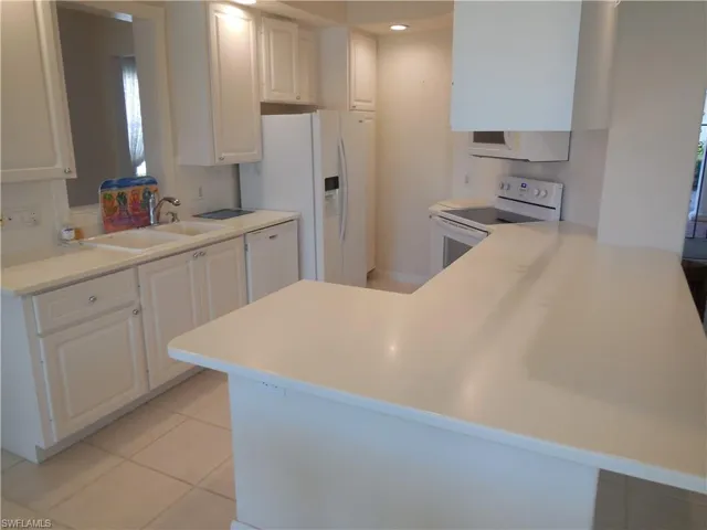 Kitchen featuring white cabinets, white appliances, a sink, and a peninsula