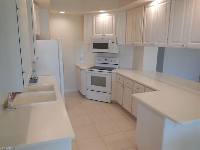 Kitchen with white appliances, light tile patterned floors, white cabinetry, light countertops, and a peninsula