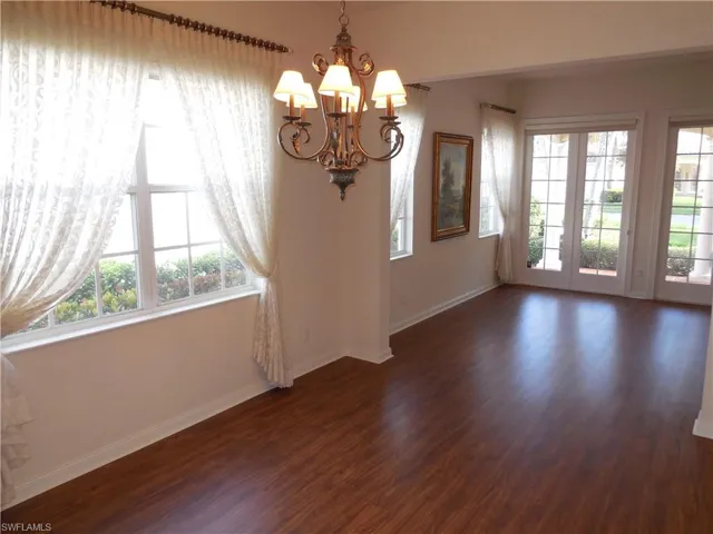 Unfurnished dining area with a notable chandelier, dark wood-style floors, and baseboards