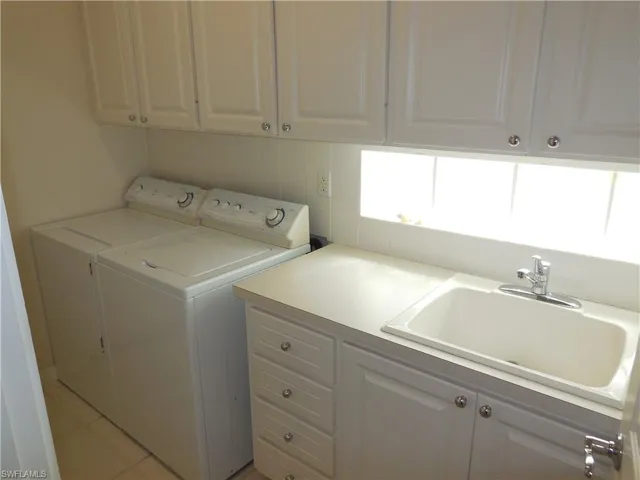 Washroom with light tile patterned floors, washer and clothes dryer, a sink, and cabinet space