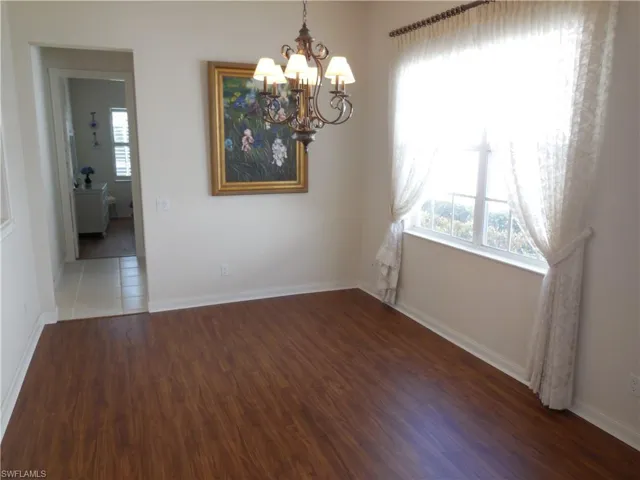Unfurnished dining area with wood finished floors, an inviting chandelier, and baseboards