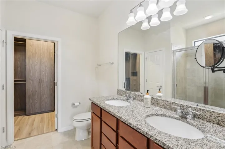 Master Suite Bathroom featuring toilet, tile flooring, walk in shower, dual sink and a walk-in closet