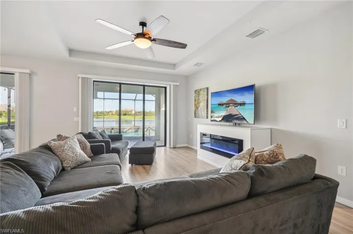 Living room with ceiling fan, electric fireplace, laminate flooring, tray ceiling, and a beautiful view of the water from the lanai